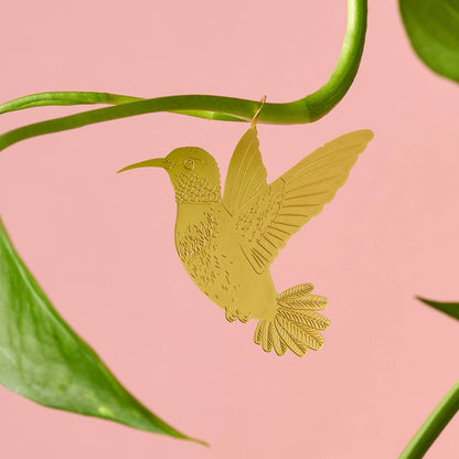 Brass hummingbird plant animal hanging from a plant, looking as if it is flying adding a playful touch to houseplants, a perfect gift for plant enthusiasts, available for purchase from The Petal and Plant Company. Pink background