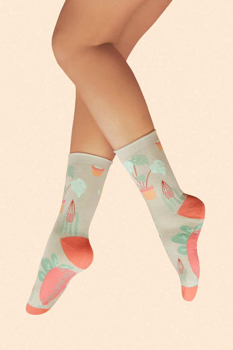 Feet wearing Thriving House Plants Ankle Socks in a coconut-coloured base with orange heels and toes, featuring green, orange, and pink houseplant designs, a delightful gift option available from The Petal and Plant Company
