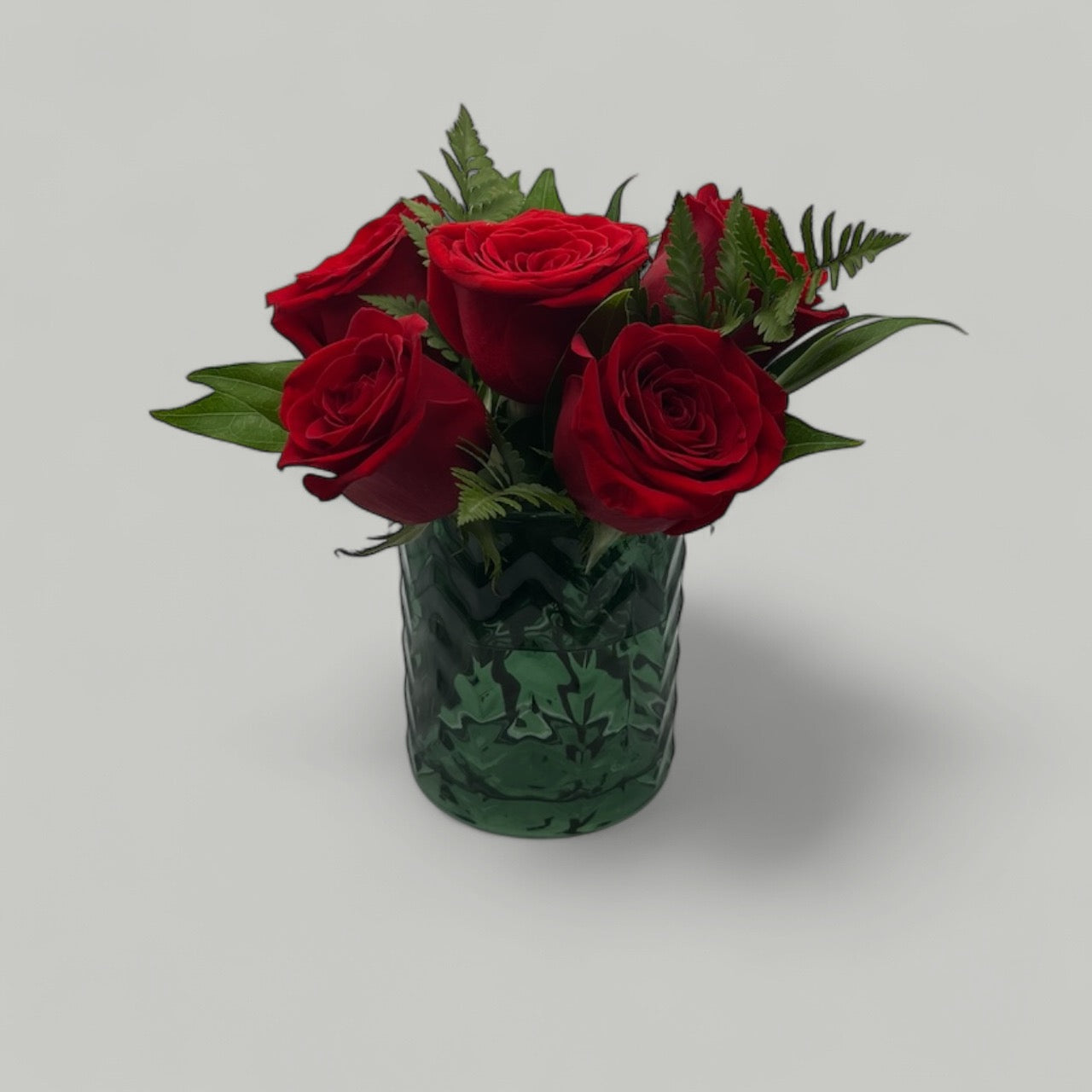Dark bottle green short glass vase with decorative 3D chevrons, filled with vibrant red roses, available for purchase from The Petal and Plant Company.