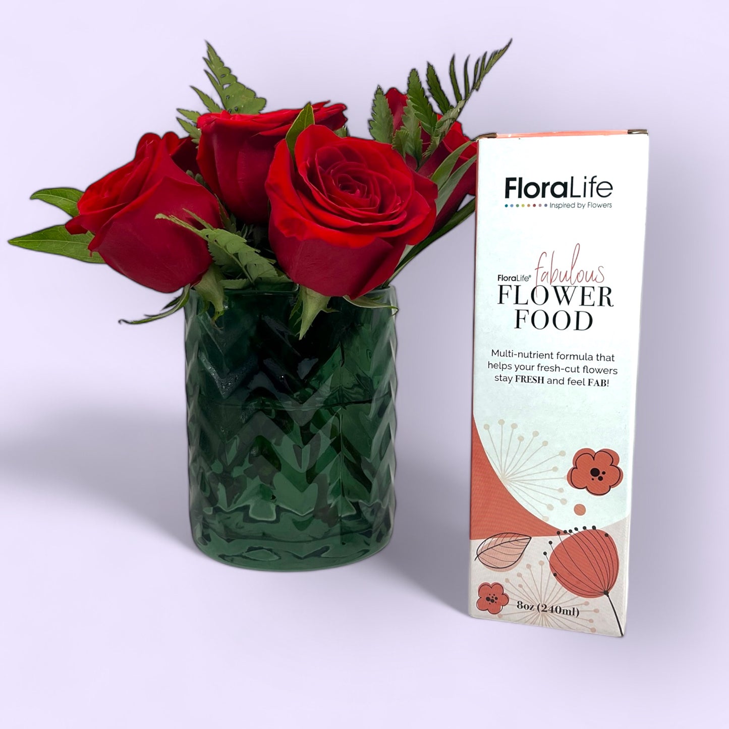 One box of Floralife flower care food on the right, with a dark bottle green short vase filled with red roses on the left, set against a purple background, showcasing floral care products and vases for sale.