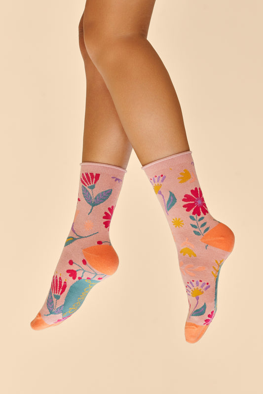 Two feet wearing Watercolour Flowers Ankle Socks in a pink base with orange heels and toes, featuring a blue, pink, yellow, and purple floral design, a stylish gift option available from The Petal and Plant Company