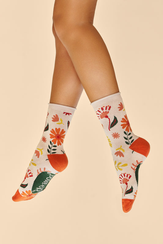 Feet wearing Watercolour Flowers Ankle Socks in cream with orange heels and toes, decorated with an orange, yellow, and green floral design, a charming gift available from The Petal and Plant Company.