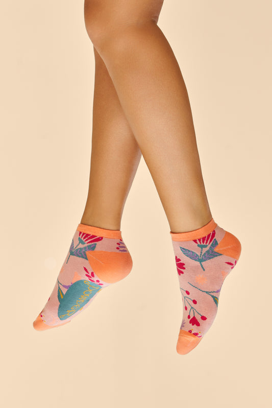 Two Feet wearing Watercolour Flowers Trainer Socks in a pink base with orange heels and toes, adorned with blue, pink, yellow, and purple floral patterns, perfect as a gift or treat from The Petal and Plant Company