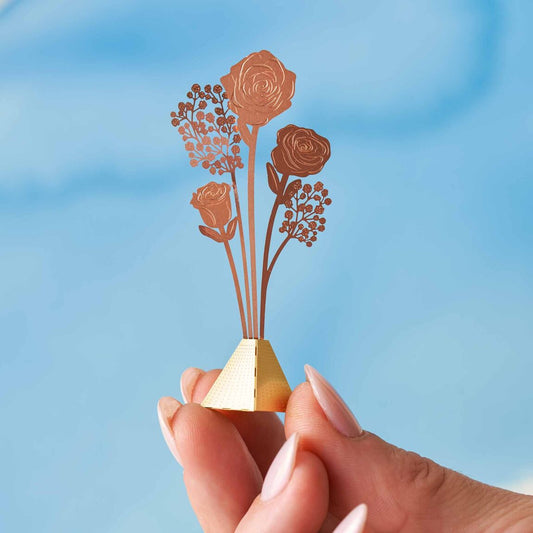 Tiny bouquet of brass roses held between a finger and thumb, showcasing its delicate size, available for purchase from The Petal and Plant Company
