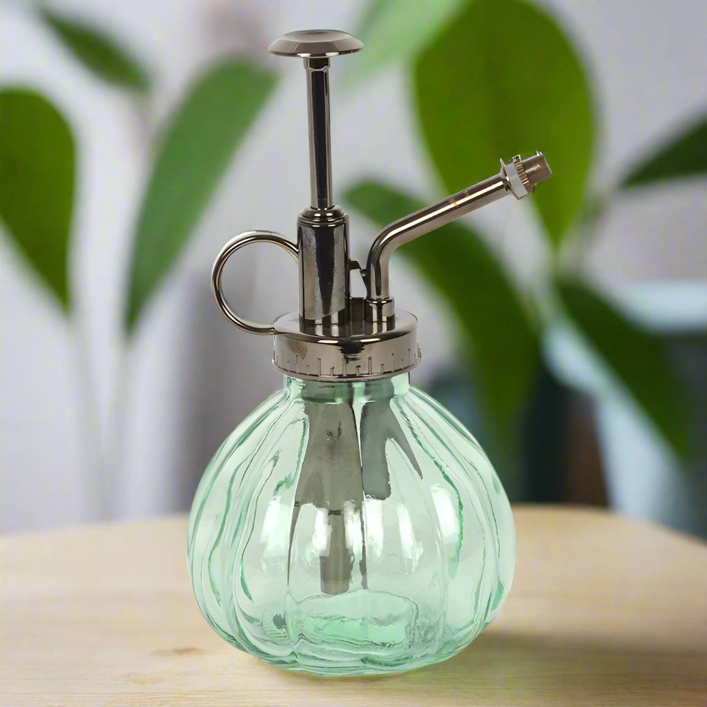 Green bulbous water mister designed for keeping plants hydrated, displayed on a wooden table, available for purchase from The Petal and Plant Company.